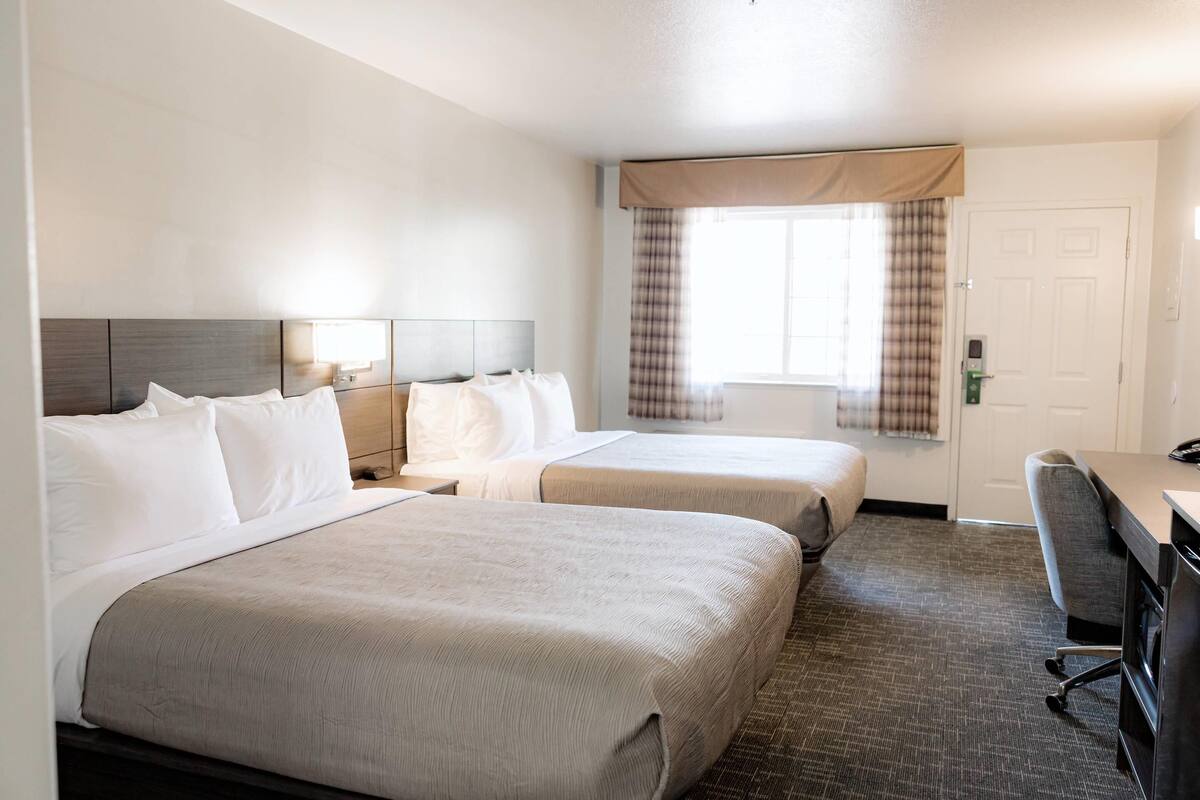 A hotel room with two beds, a desk, and a chair.