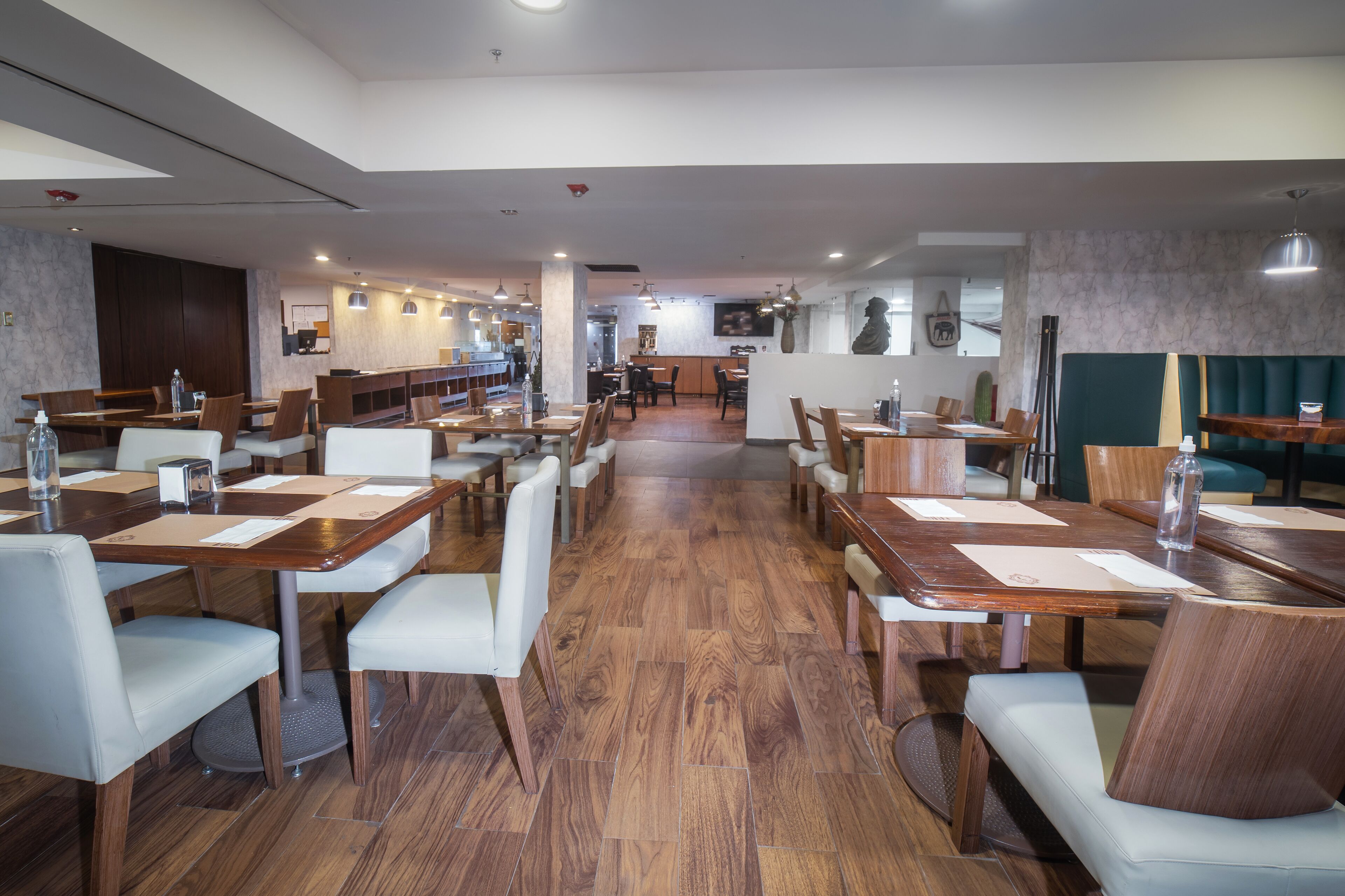 Een ruim restaurant met houten tafels, witte stoelen, een marmeren wand en een groene zithoek.