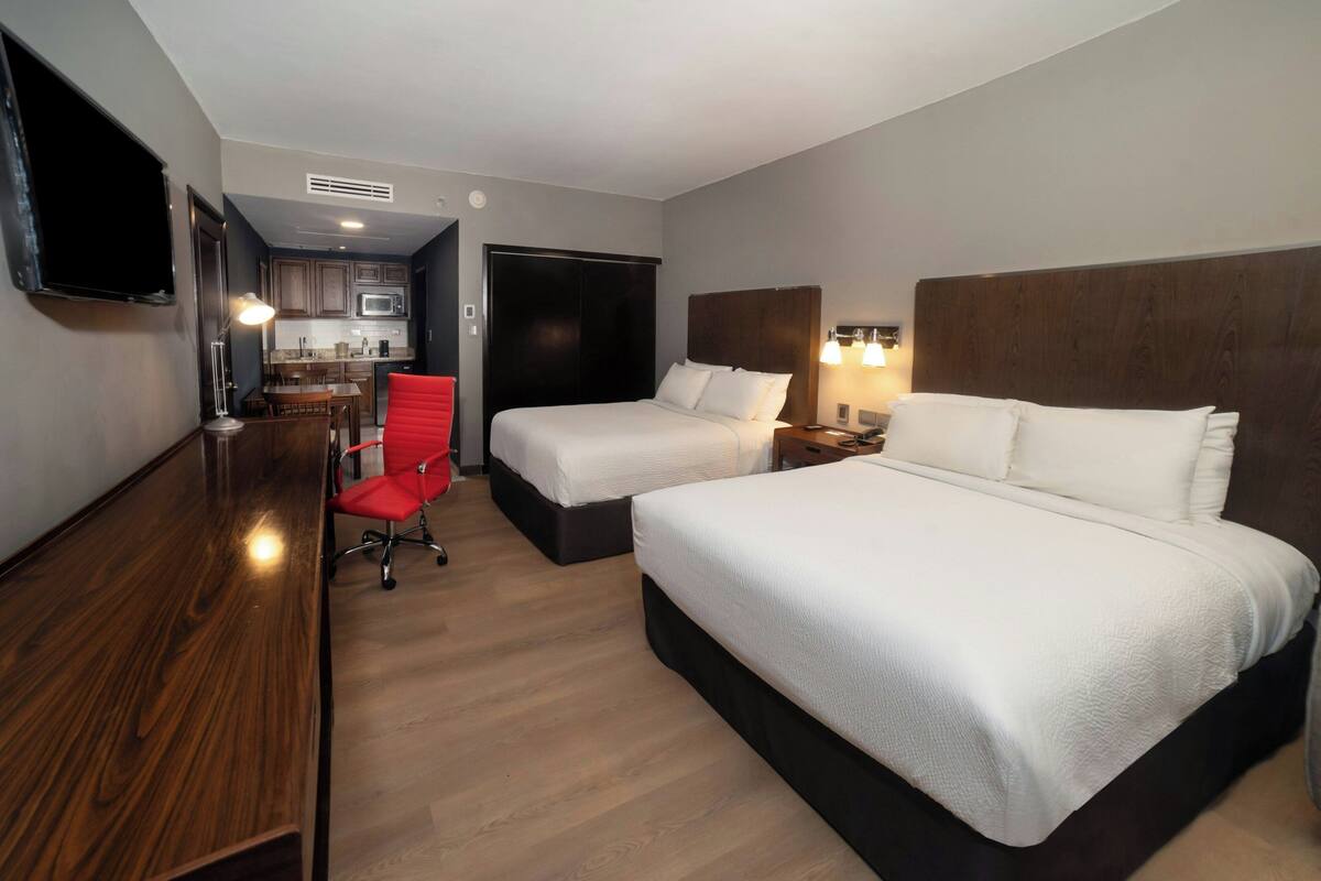 Habitación de hotel con dos camas, un escritorio, una silla, un televisor y un espacio con cocina.