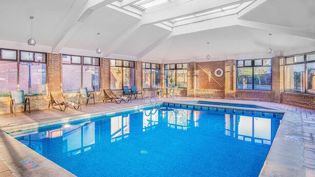 An indoor swimming pool with clear blue water, surrounded by brick walls and large windows. - Four Points by Sheraton Saltillo (Saltillo)