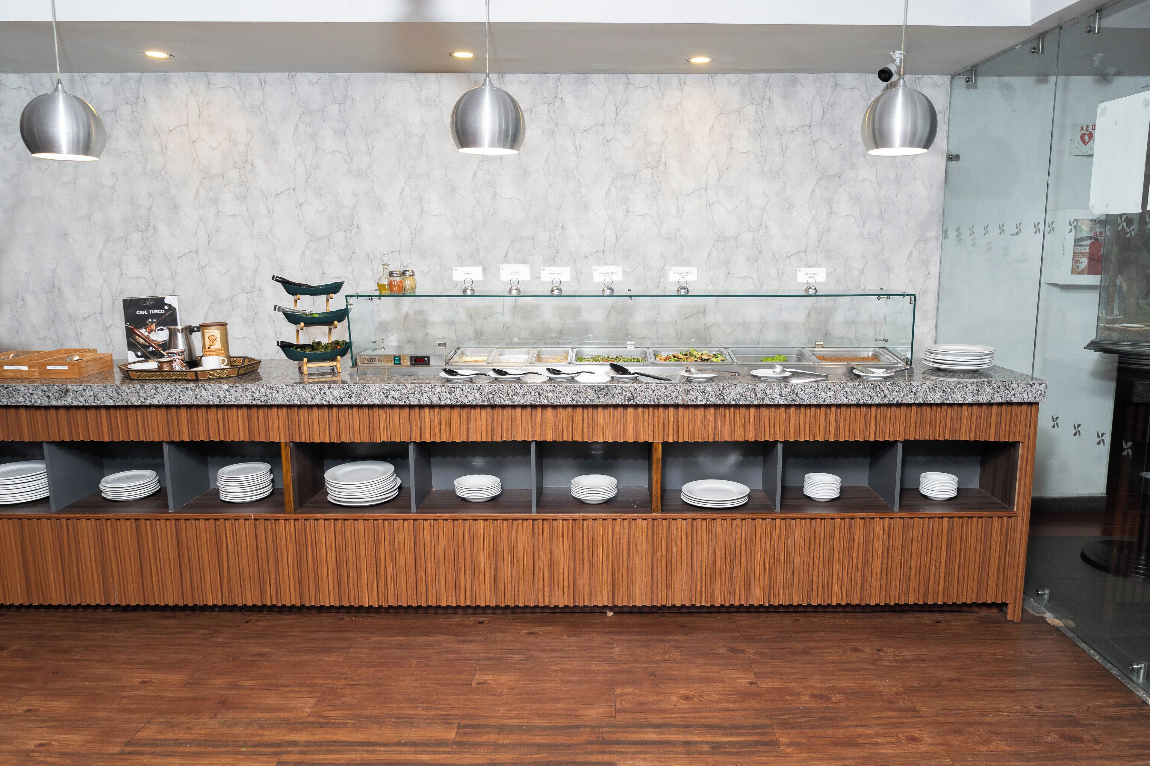 Zona de buffet con pared de mármol, estantes de madera y lámparas colgantes de metal.