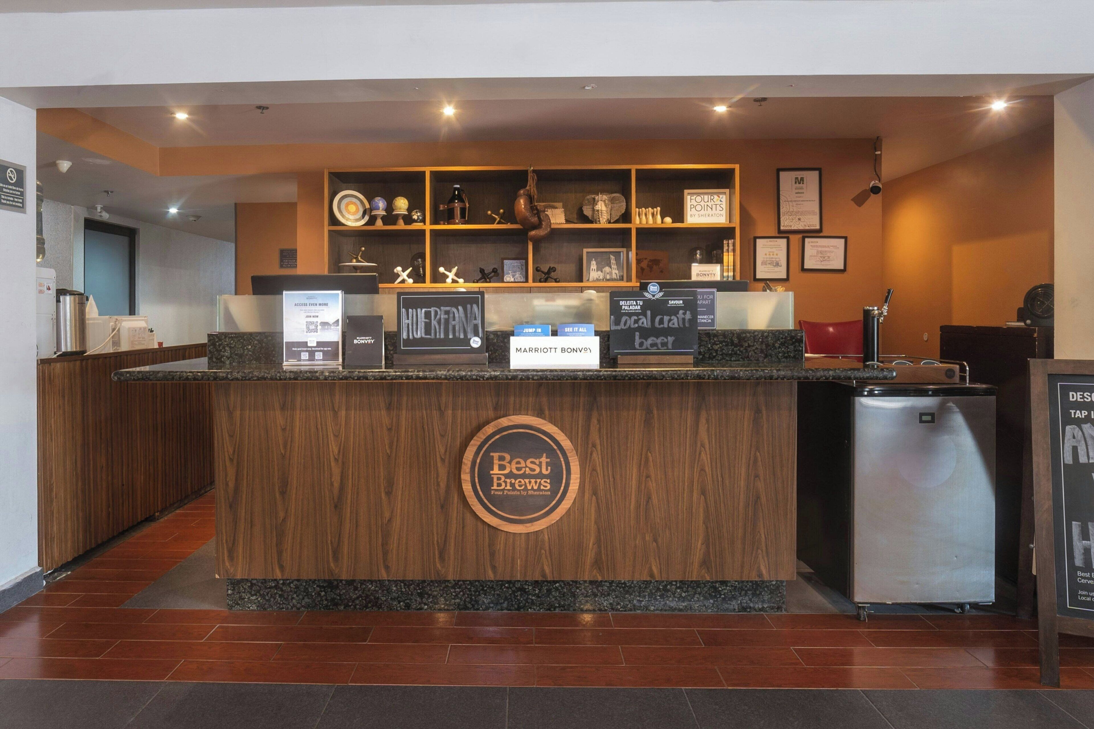 A reception area with a wooden counter, a digital screen, and a refrigerator.