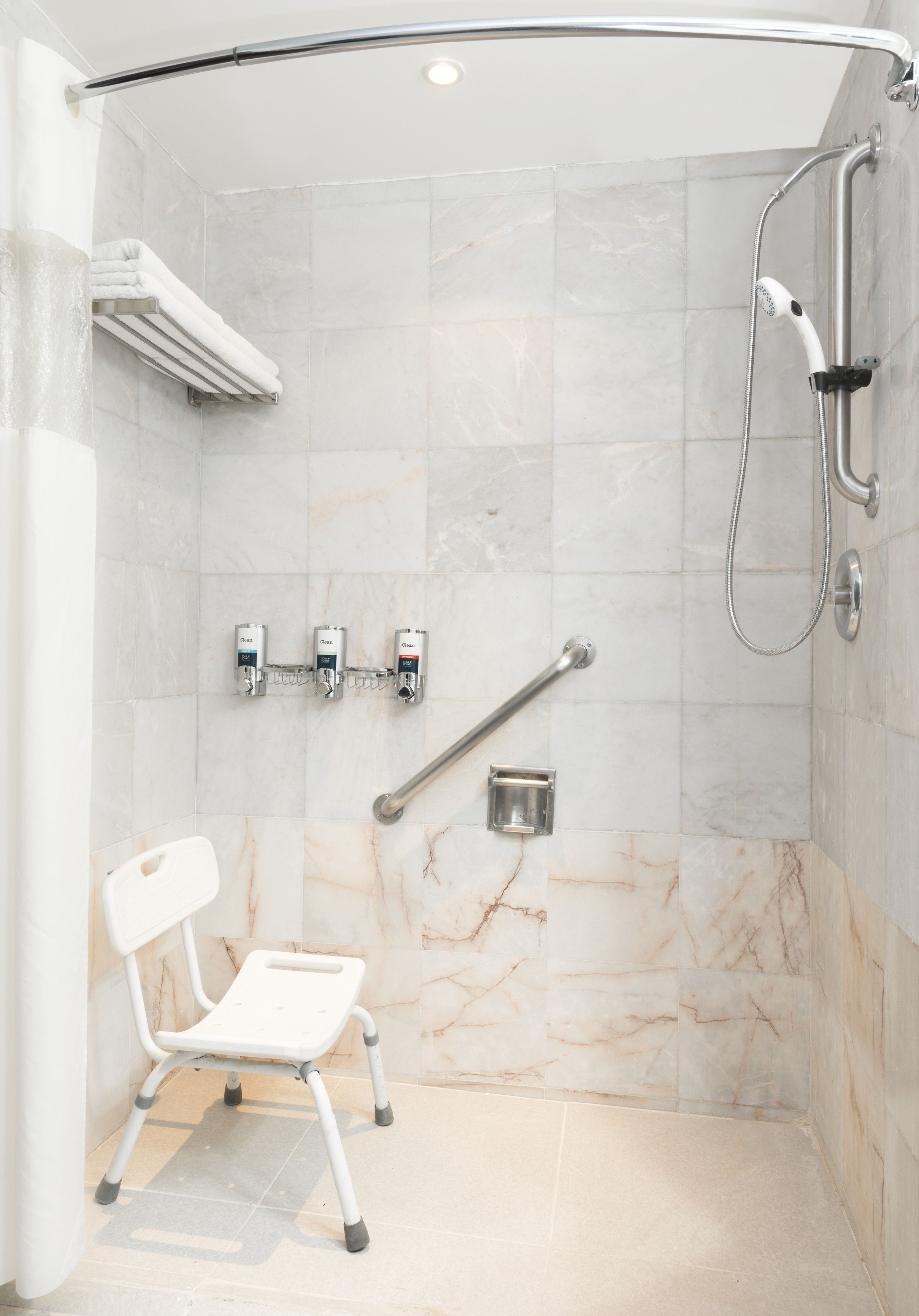 A modern shower area with a handheld showerhead, a grab bar, and a white chair.