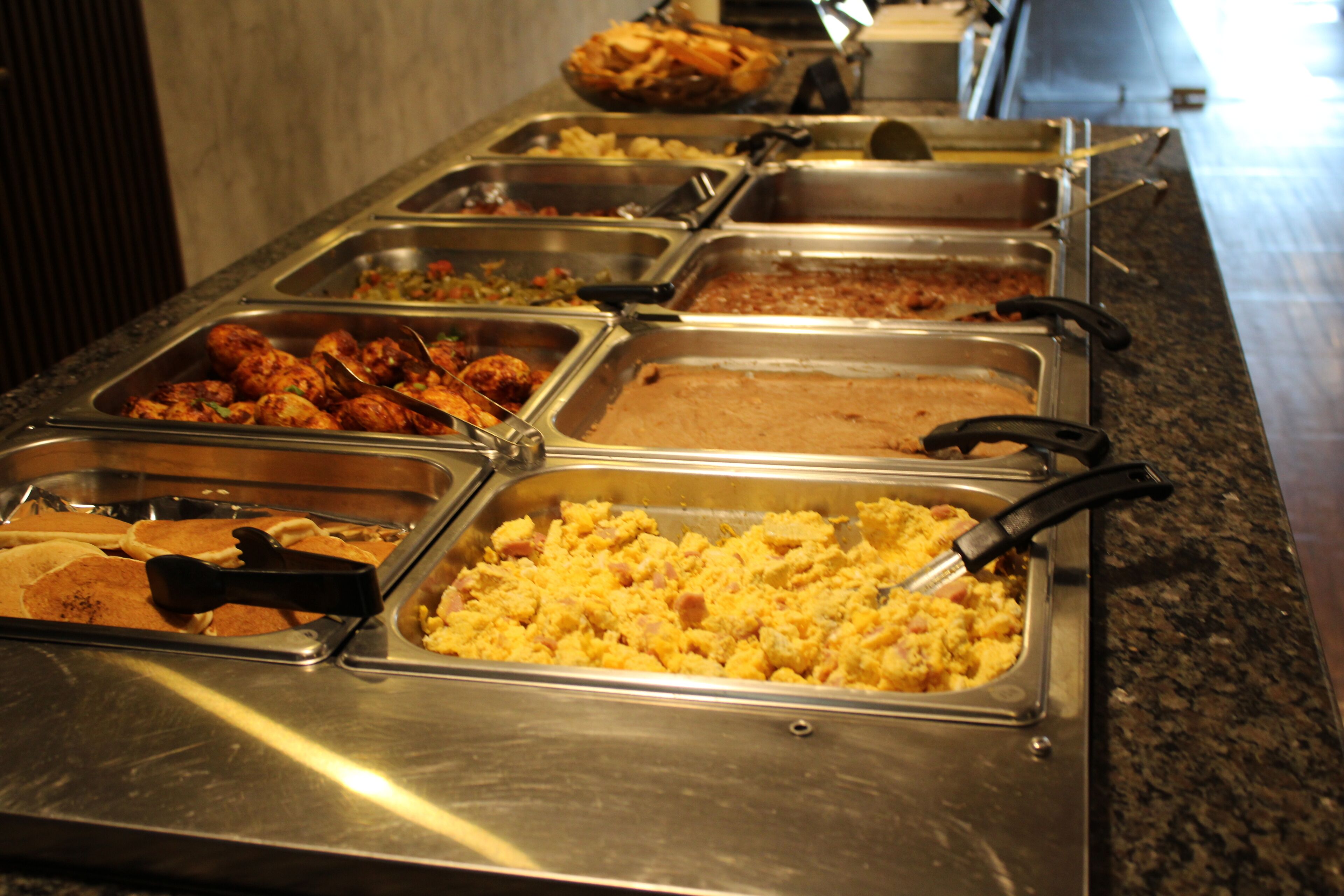 Un bufé con diversas opciones de comida, incluyendo huevos revueltos, pollo y otros platos.