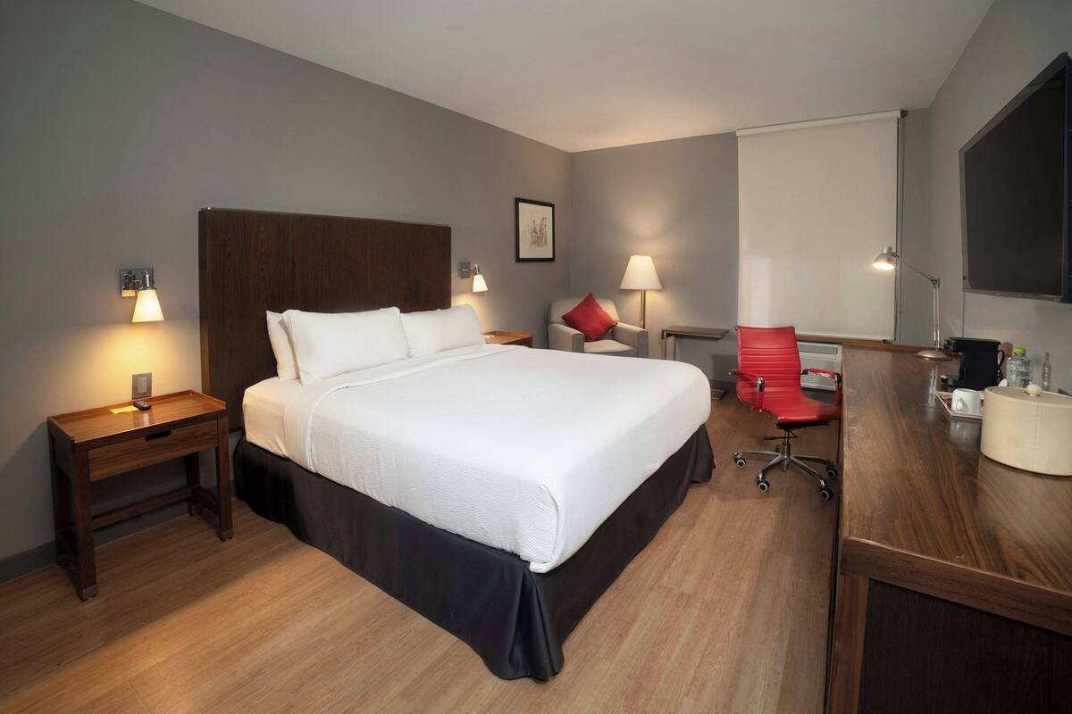 Una habitación de hotel con una cama grande, mesitas de noche, un escritorio con una silla y un televisor.