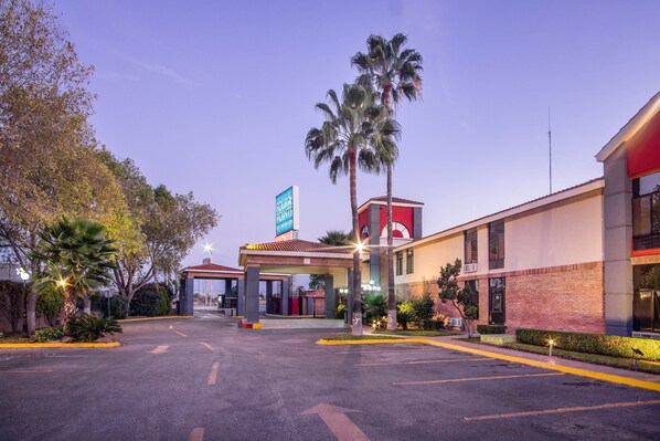 A hotel with a red and beige facade, palm trees, and a clear sky. - Four Points by Sheraton Saltillo (Saltillo)