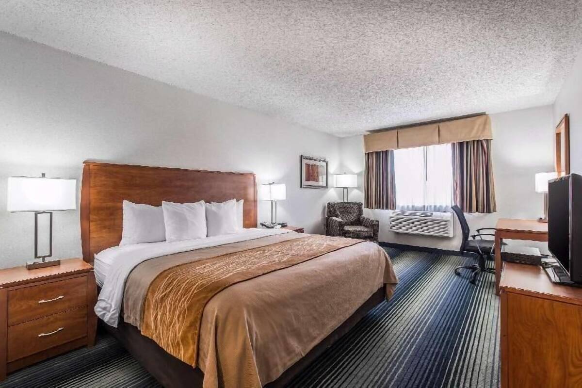 A hotel room with a large bed, bedside lamps, a desk with a computer, and a television.