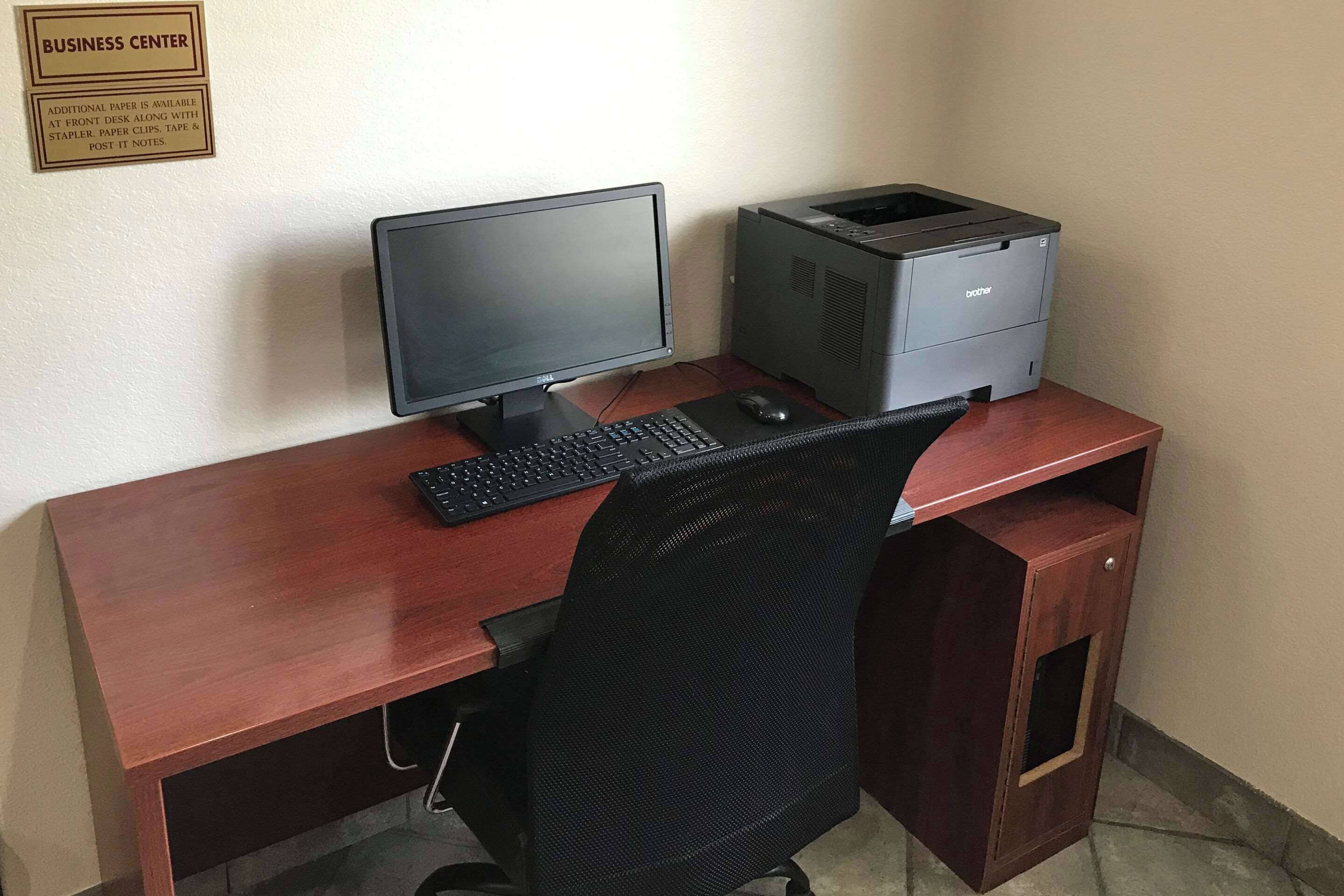 A wooden desk with a computer monitor, keyboard, and printer.