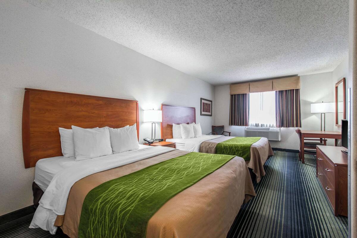 A hotel room with two beds, a desk, a chair, a lamp, and a TV.