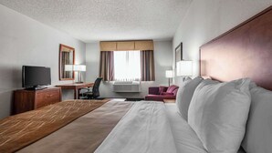 Habitación de hotel con cama, escritorio, televisor, silla y ventana con cortinas.