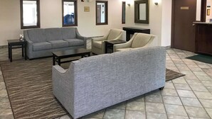 Un hall de hotel con un sofá gris, una silla, una mesita y un espejo en la pared.