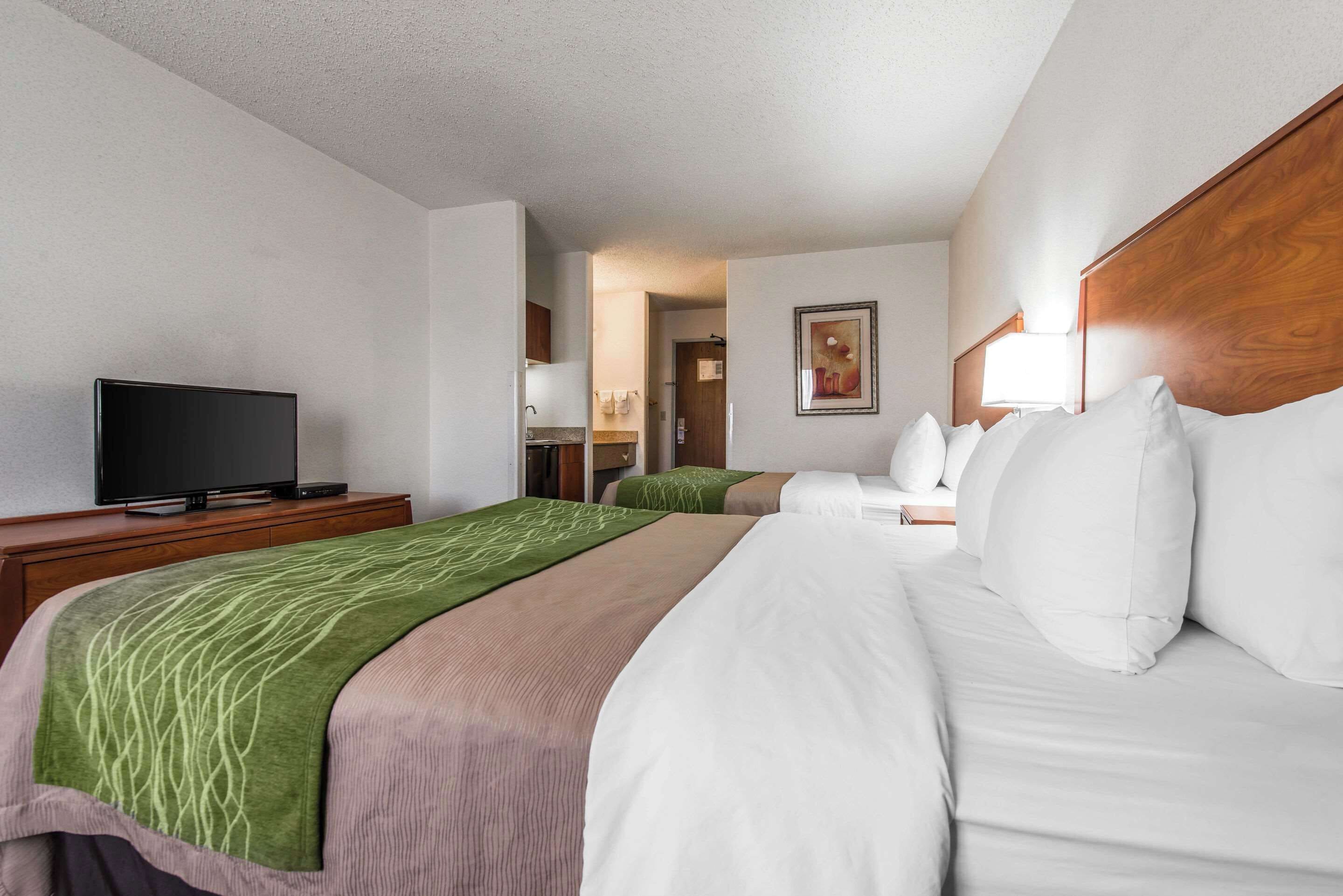 A hotel room with a bed, a TV on a stand, a wooden headboard, and a painting on the wall.