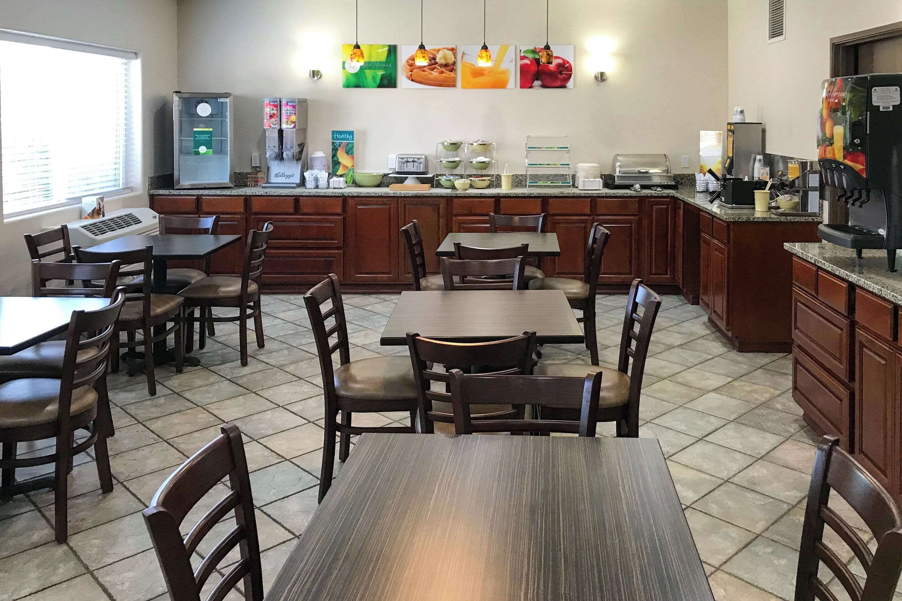 Un comedor de hotel con mesas y sillas de madera, una estación de café y un refrigerador.