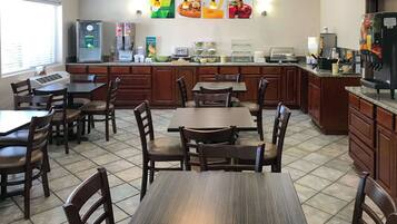 Un comedor de hotel con mesas y sillas de madera, una estación de café y un refrigerador.