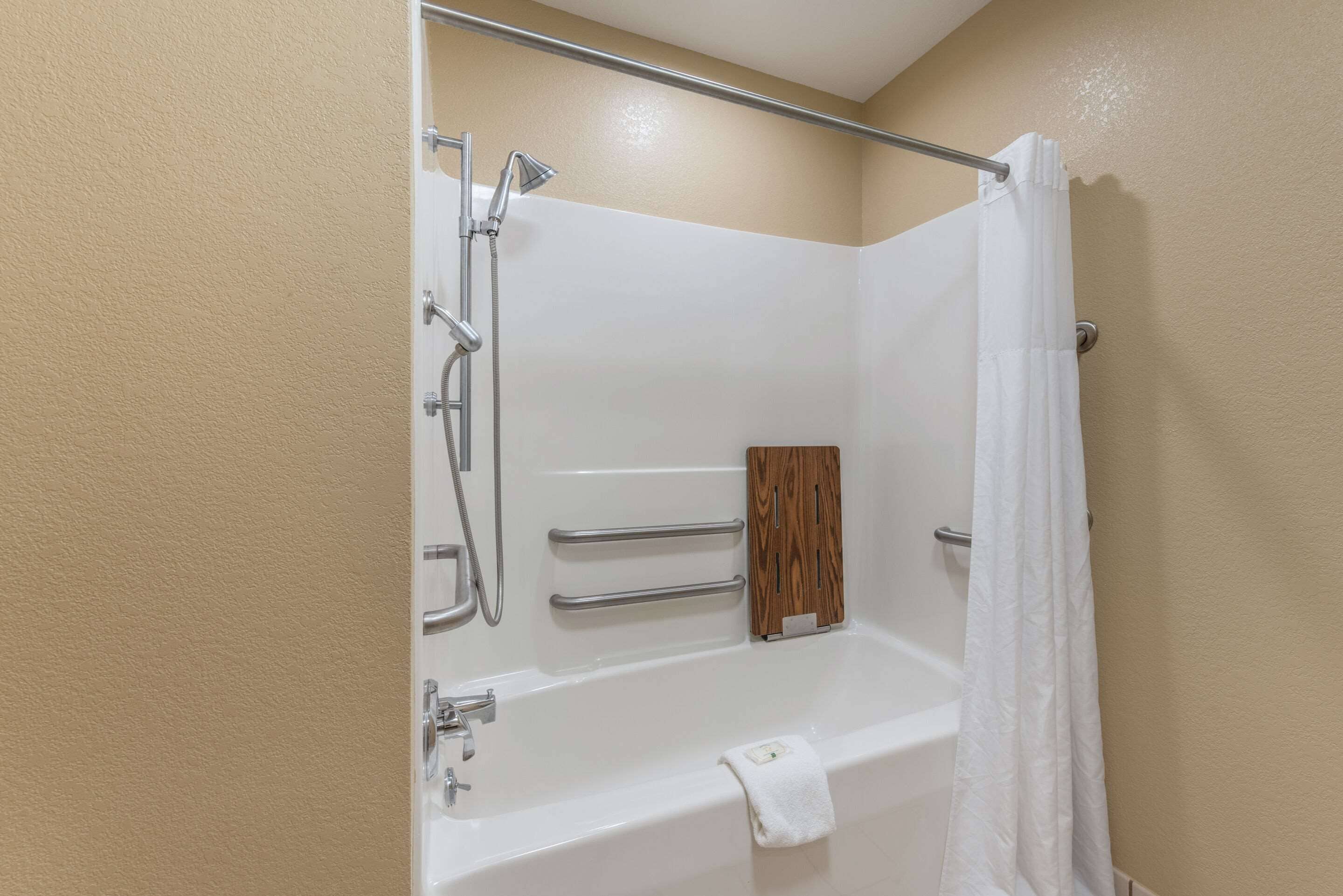 A bathroom with a bathtub, shower, and grab bars.