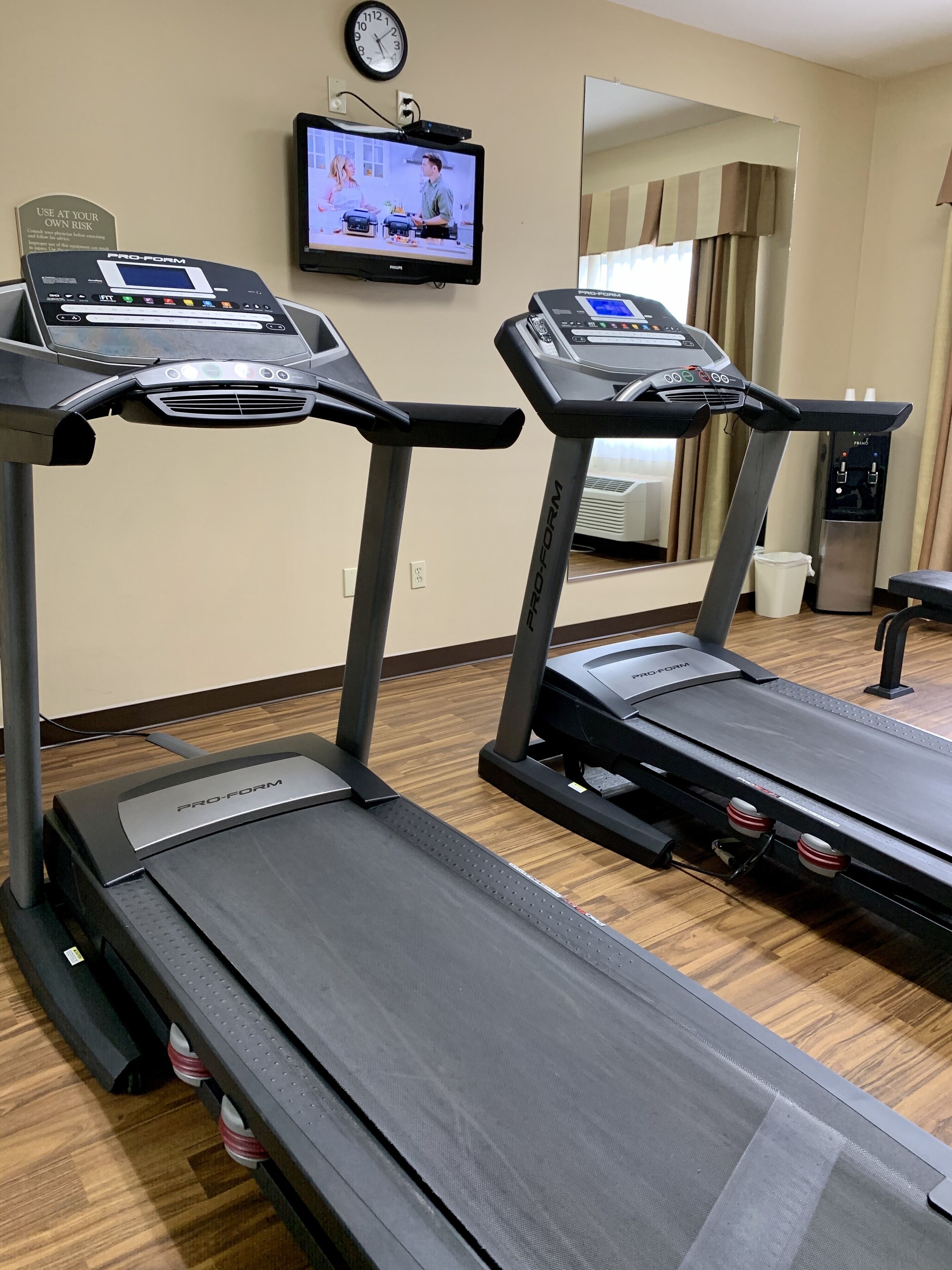 A hotel fitness room with two ProForm treadmills, a television, and a water dispenser.