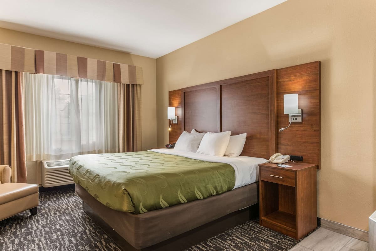 Una habitación de hotel con una cama grande, una mesita de noche con un teléfono, una silla y una ventana con cortinas.