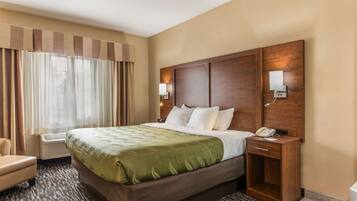 Quarto de hotel com uma cama grande, mesa de cabeceira com telefone, uma cadeira e uma janela com cortinas.