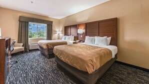 A hotel room with two beds, a desk, a chair, and a window with curtains. - Quality Inn & Suites Hendersonville - Flat Rock (Flat Rock)