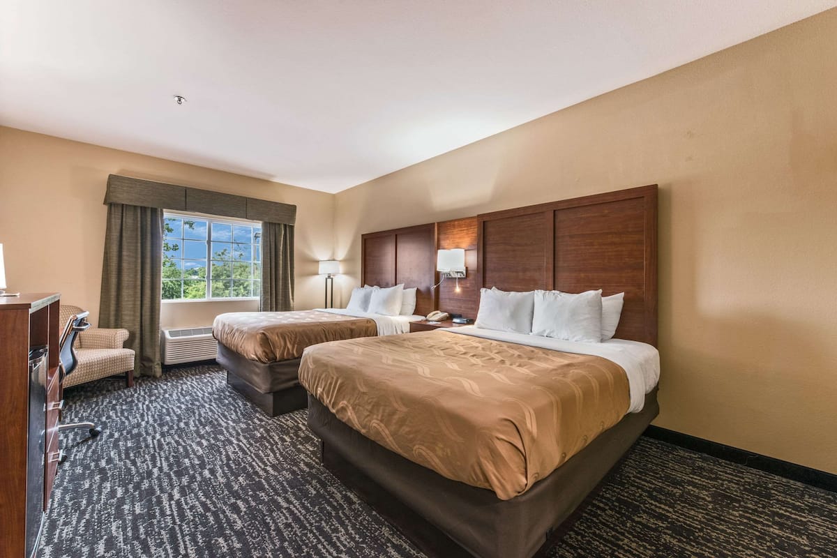 Habitación de hotel con dos camas, un escritorio, una silla y una ventana con cortinas.