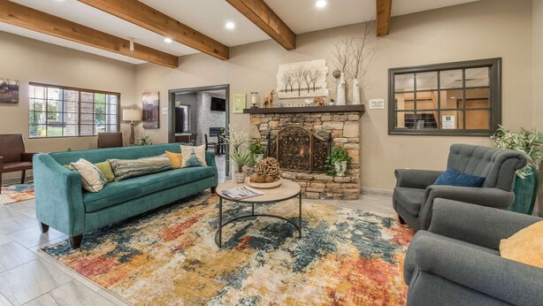 A spacious living room with a stone fireplace, wooden beams, a teal sofa, and a gray armchair. - Quality Inn & Suites Hendersonville - Flat Rock (Flat Rock)