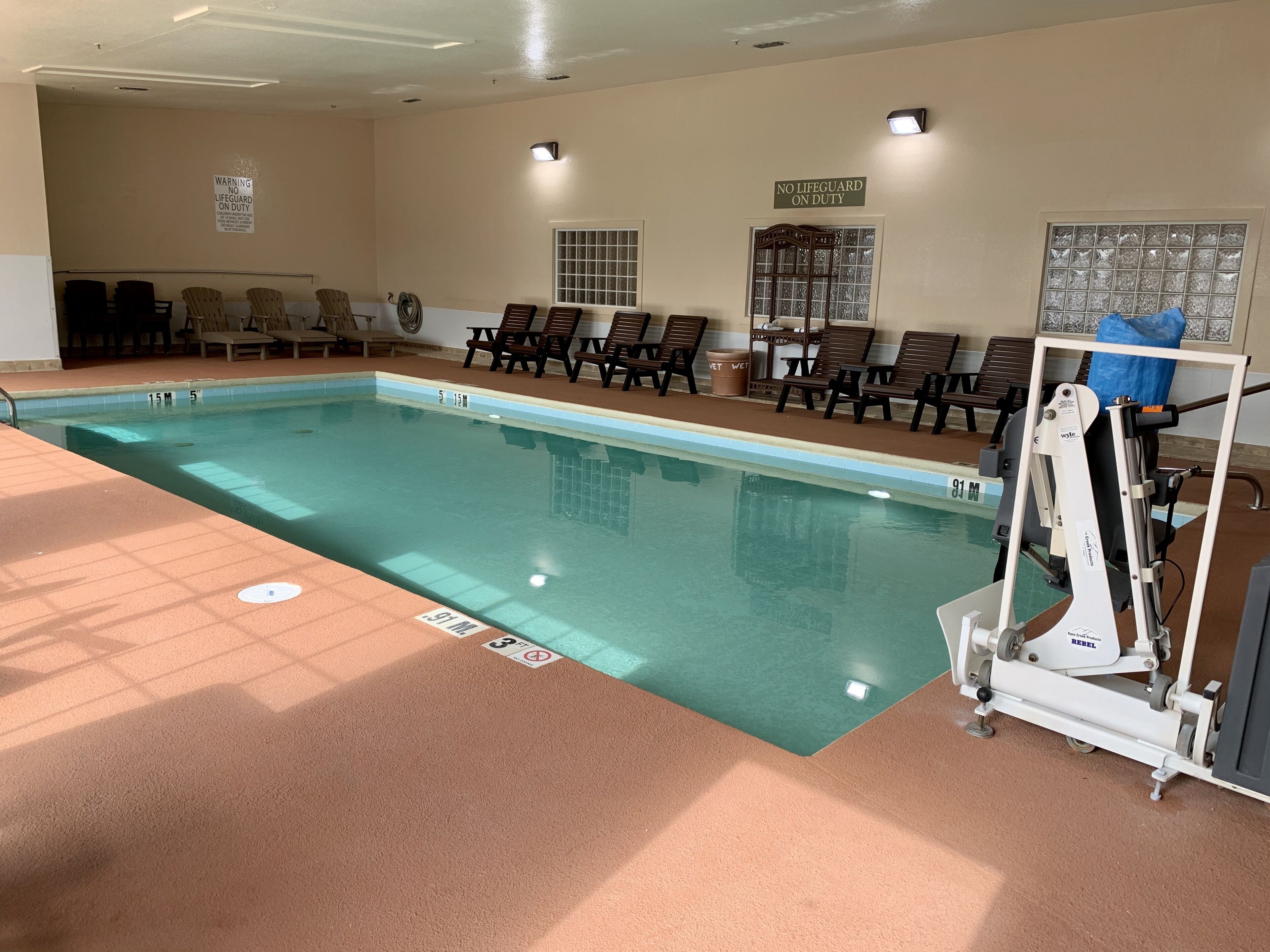 An indoor swimming pool with lounge chairs, a lifeguard stand, and a sign indicating no lifeguard on duty.