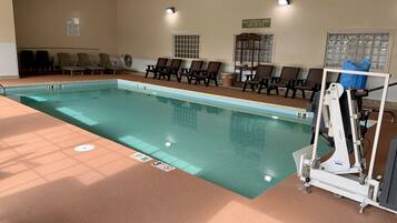 An indoor swimming pool with lounge chairs, a lifeguard stand, and a sign indicating no lifeguard on duty.