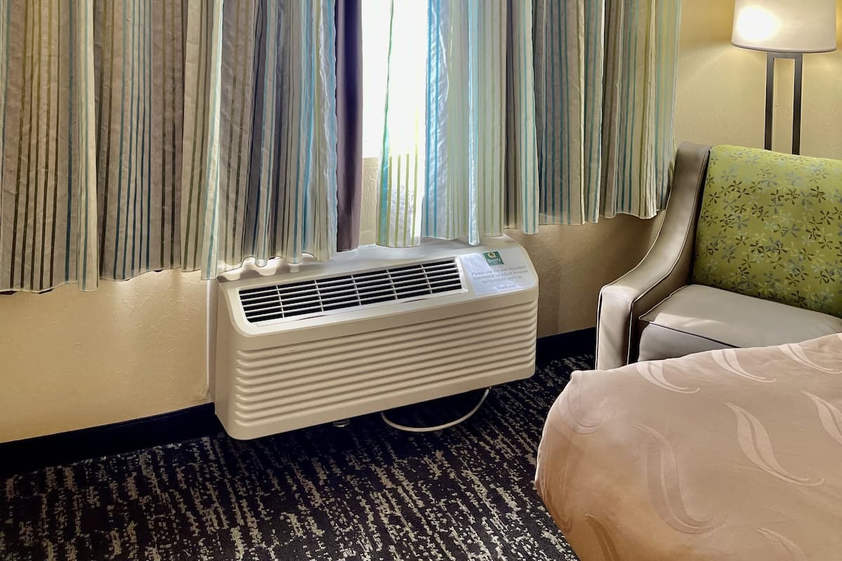 Una habitación de hotel con cortinas a rayas, un calentador portátil, una cama, una silla y una lámpara.
