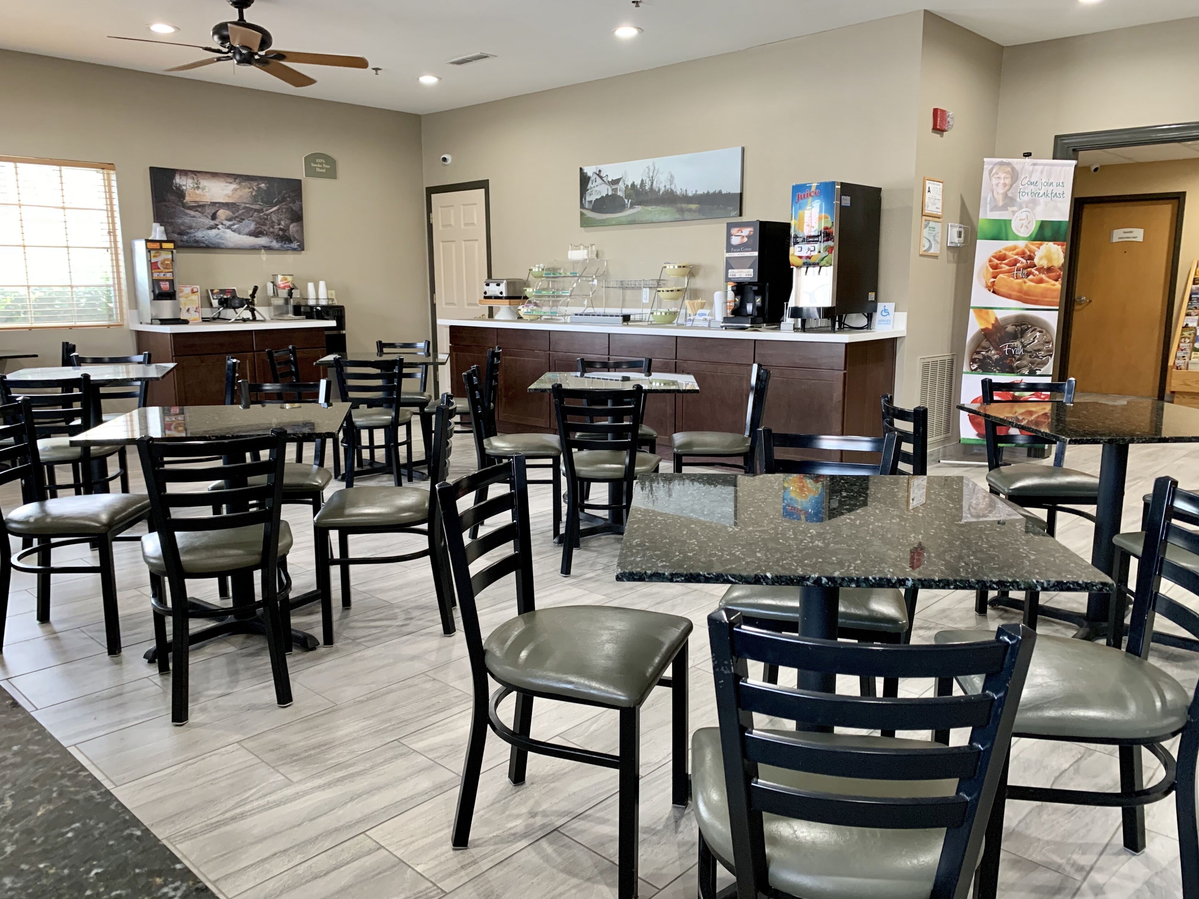 A restaurant with multiple tables and chairs, a kitchen area, and a counter with a menu board.