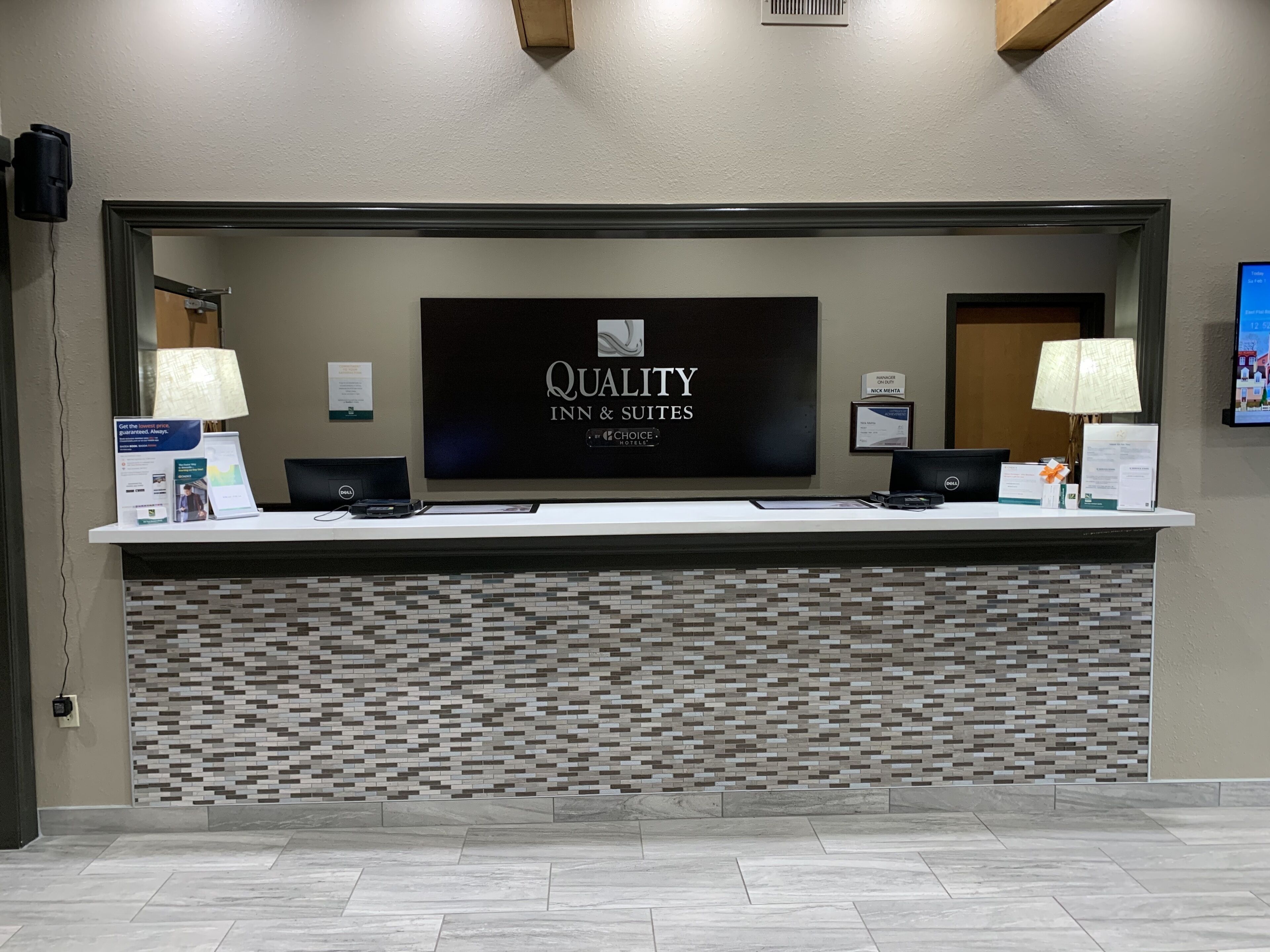 Un mostrador de recepción con un letrero que dice "Quality Inn & Suites" y una pared de azulejos debajo.
