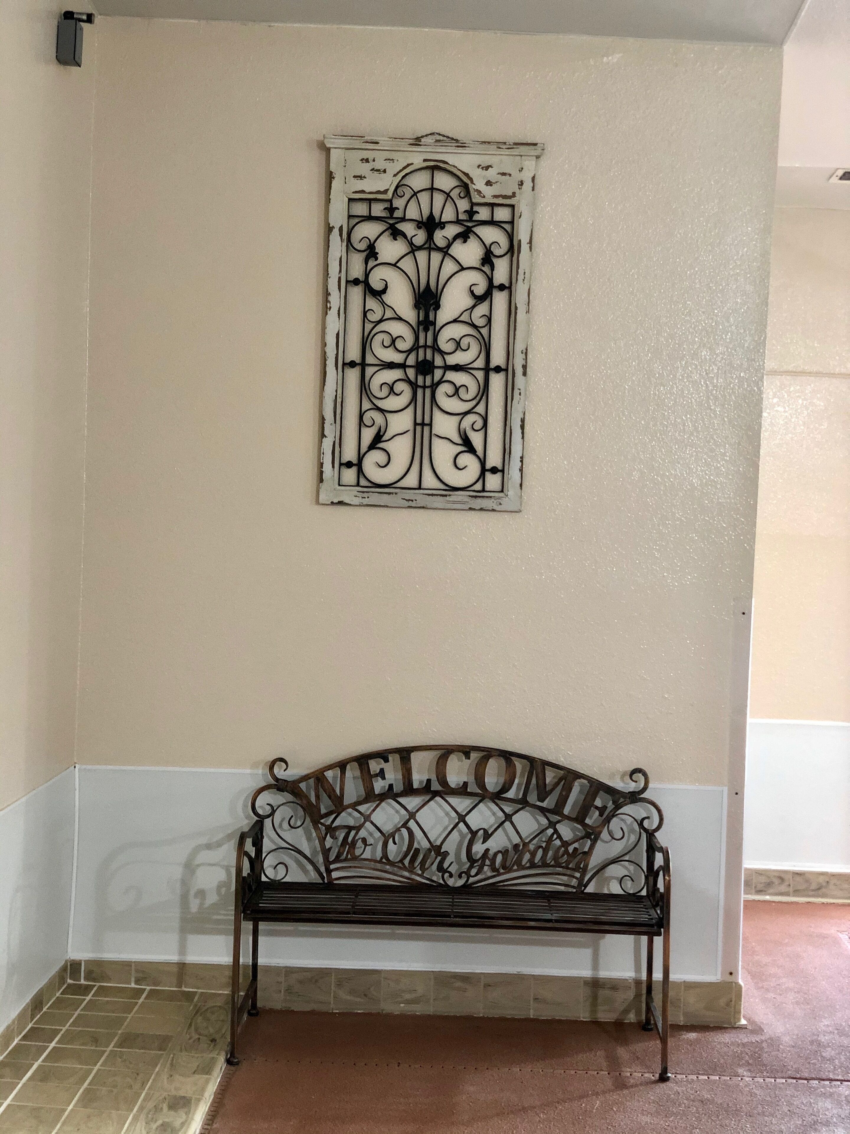 A bench with a "WELCOME" sign above it, set against a wall with a decorative window.
