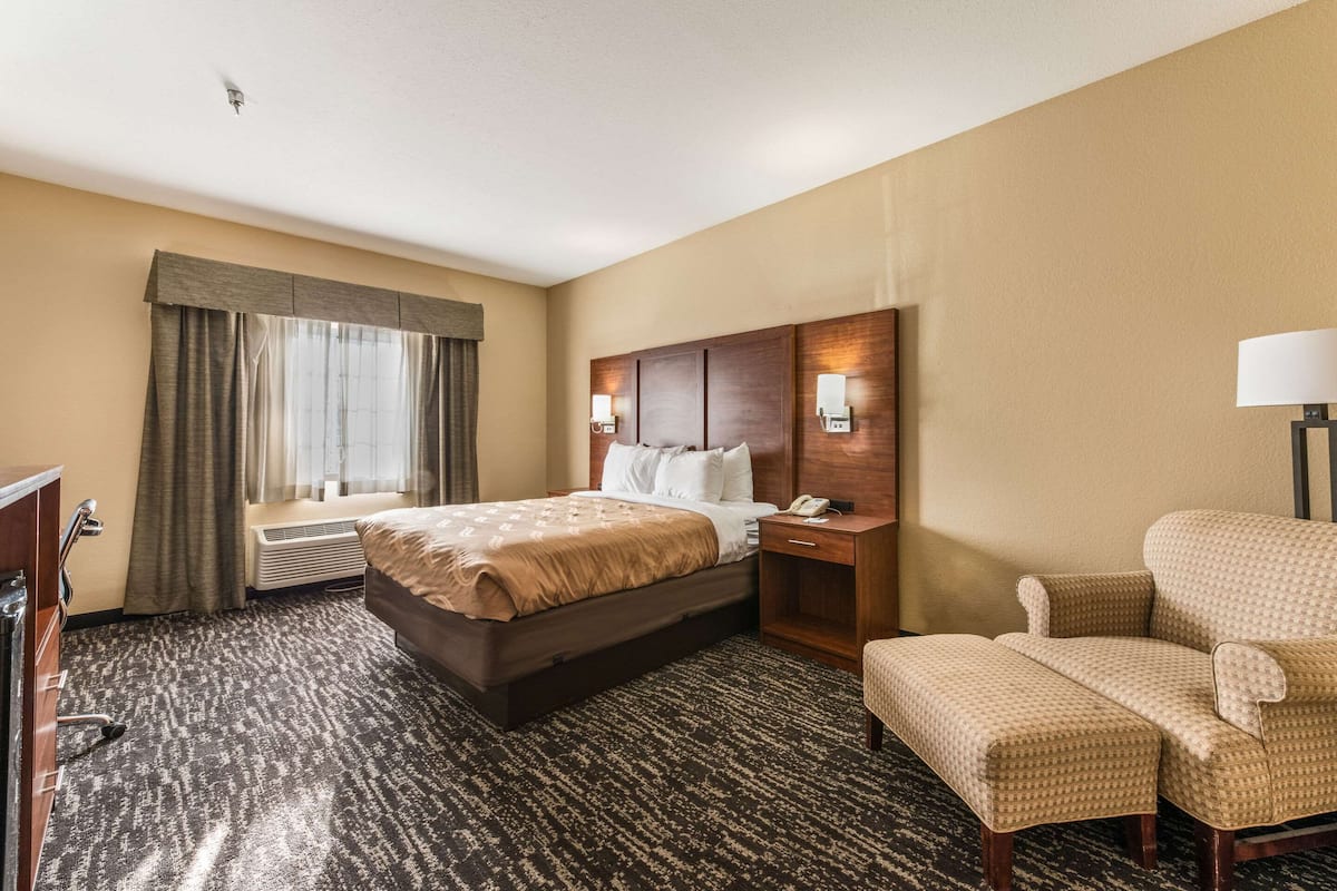Habitación de hotel con una cama grande, un escritorio con teléfono, una silla y una ventana con cortinas.