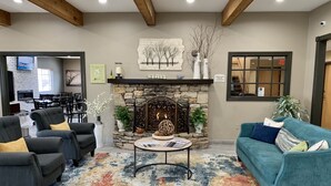 A cozy living room with a fireplace, comfortable seating, and a dining area in the background. - Quality Inn & Suites Hendersonville - Flat Rock (Flat Rock)