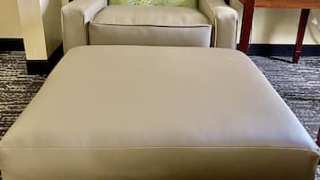Un sofá beige y un reposapiés en una habitación con alfombra estampada y una mesa de madera.