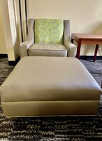 Un sofá beige y un reposapiés en una habitación con alfombra estampada y una mesa de madera.