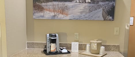 Habitació d'hotel amb zona d'esmorzar incloent una cafetera, un brollador d'aigua i un armariet petit.