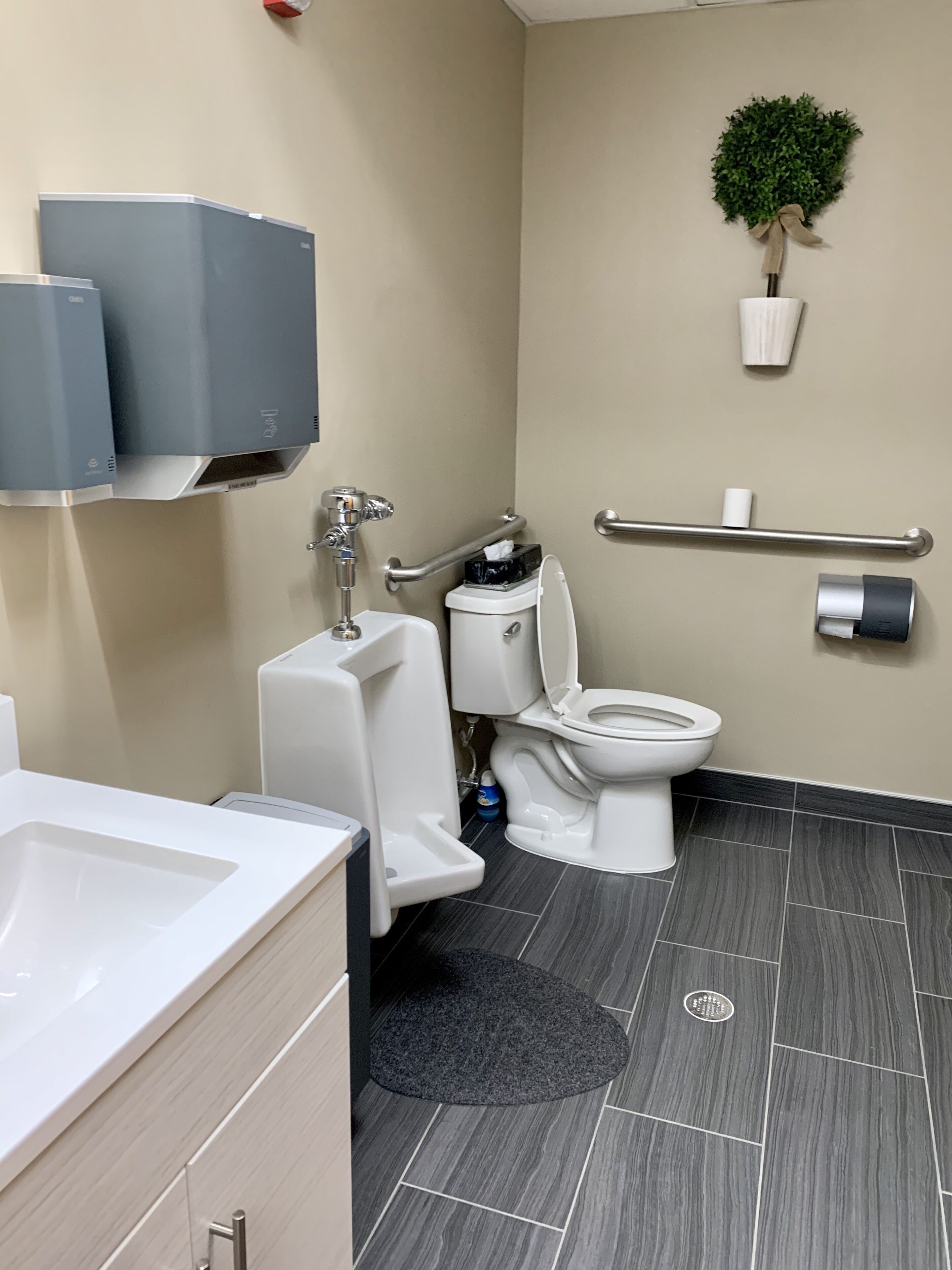 A modern bathroom with a toilet, bidet, and hand dryer. There is a small plant on the wall and a towel rack.