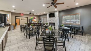 A restaurant with multiple tables and chairs, ceiling fans, and a TV mounted on the wall. - Quality Inn & Suites Hendersonville - Flat Rock (Flat Rock)