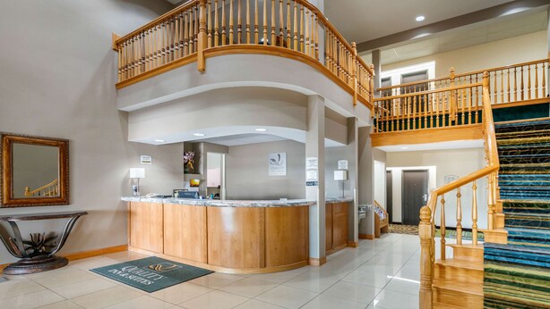 A hotel lobby with a reception desk, a staircase, and a mirror. - Quality Inn & Suites Jefferson City (Jefferson City)