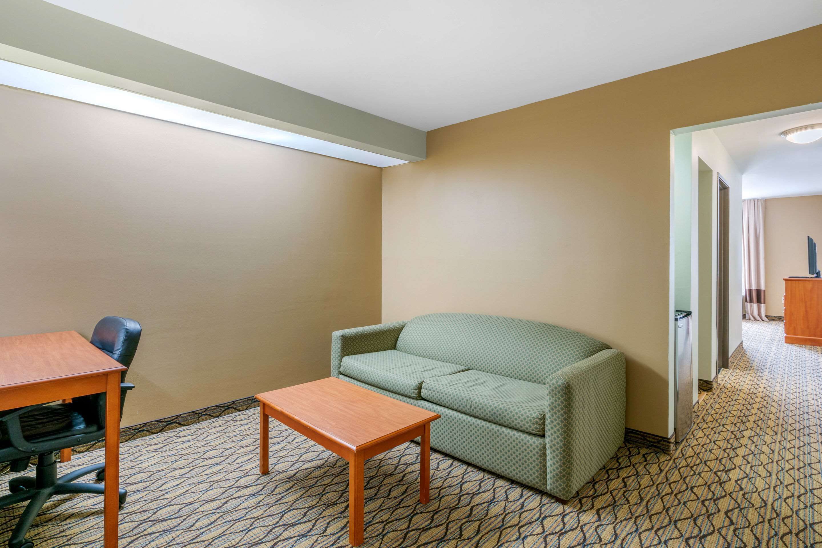 Una habitación con alfombra estampada, un sofá verde, una mesa de madera y una silla de oficina negra.