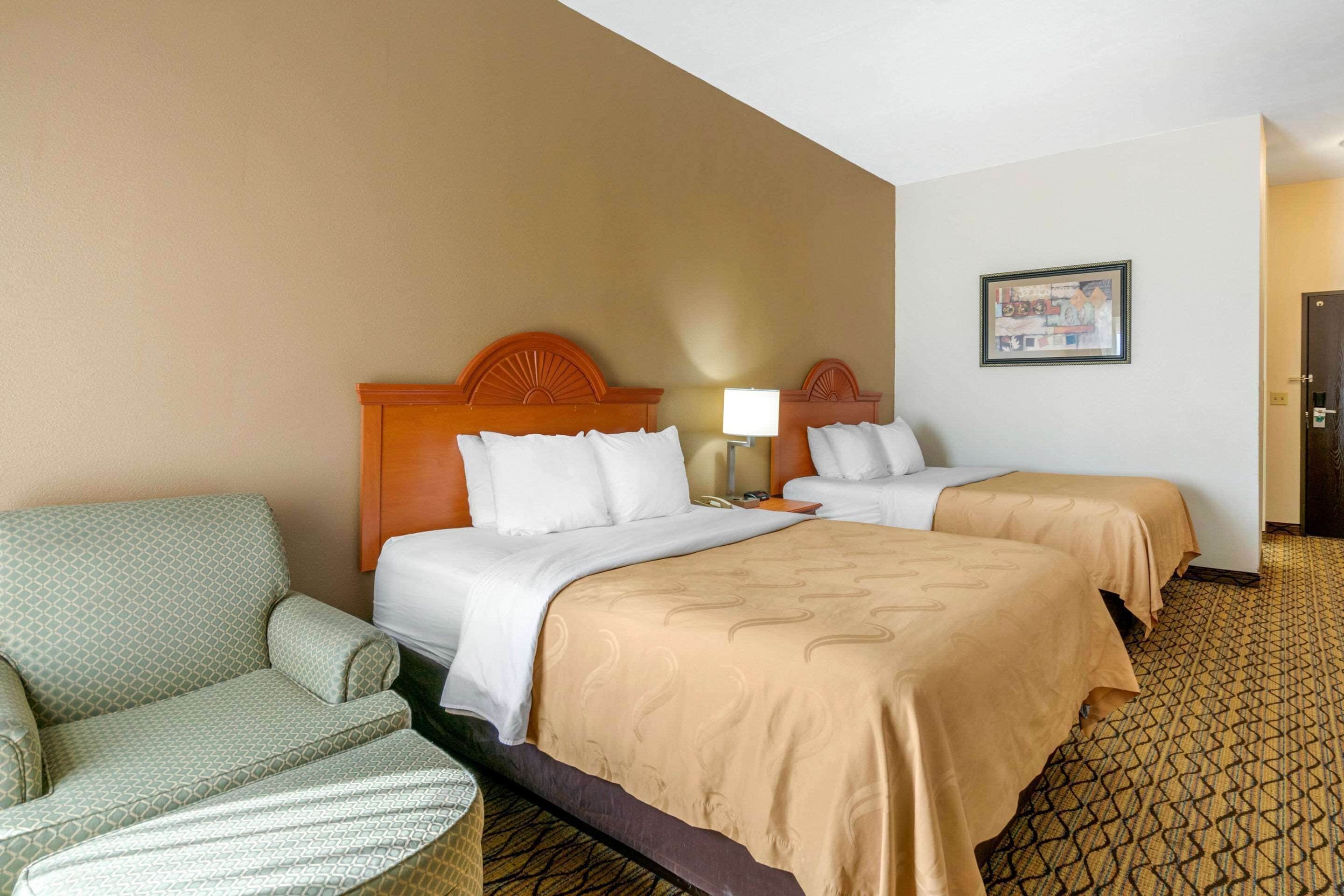 A hotel room with two beds, a sofa, a lamp, and a framed picture on the wall.