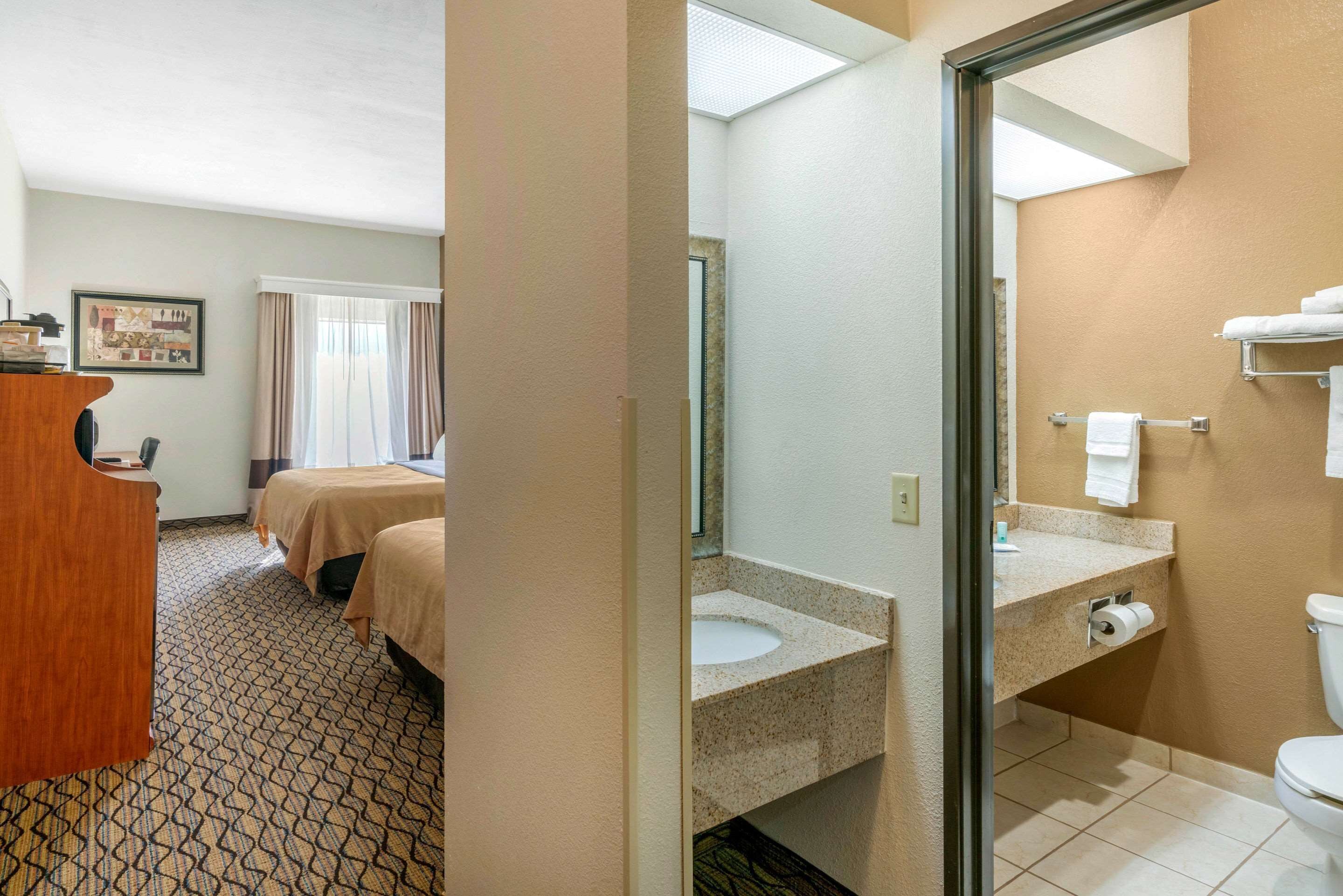 A hotel room with a bed, a desk, a bathroom with a sink and toilet, and a window with curtains.