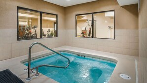 A swimming pool with a metal ladder, beige tiled walls, and two large windows reflecting exercise equipment. - Quality Inn & Suites Jefferson City (Jefferson City)