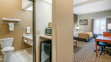 A hotel room with a toilet, a small refrigerator, a microwave, a bed, a desk, and a chair.