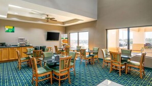A hotel dining area with multiple tables and chairs, a kitchen area with a coffee machine, and large windows offering a view of the outside. - Quality Inn & Suites Jefferson City (Jefferson City)