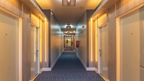 A hotel hallway with carpeted floors, wooden panel walls, and doors on both sides.