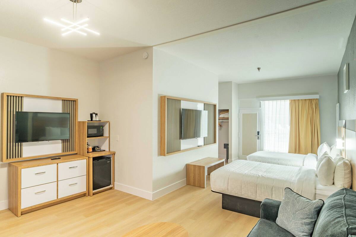 A modern hotel room with a wooden cabinet, a television, a microwave, a bed, and a sofa.