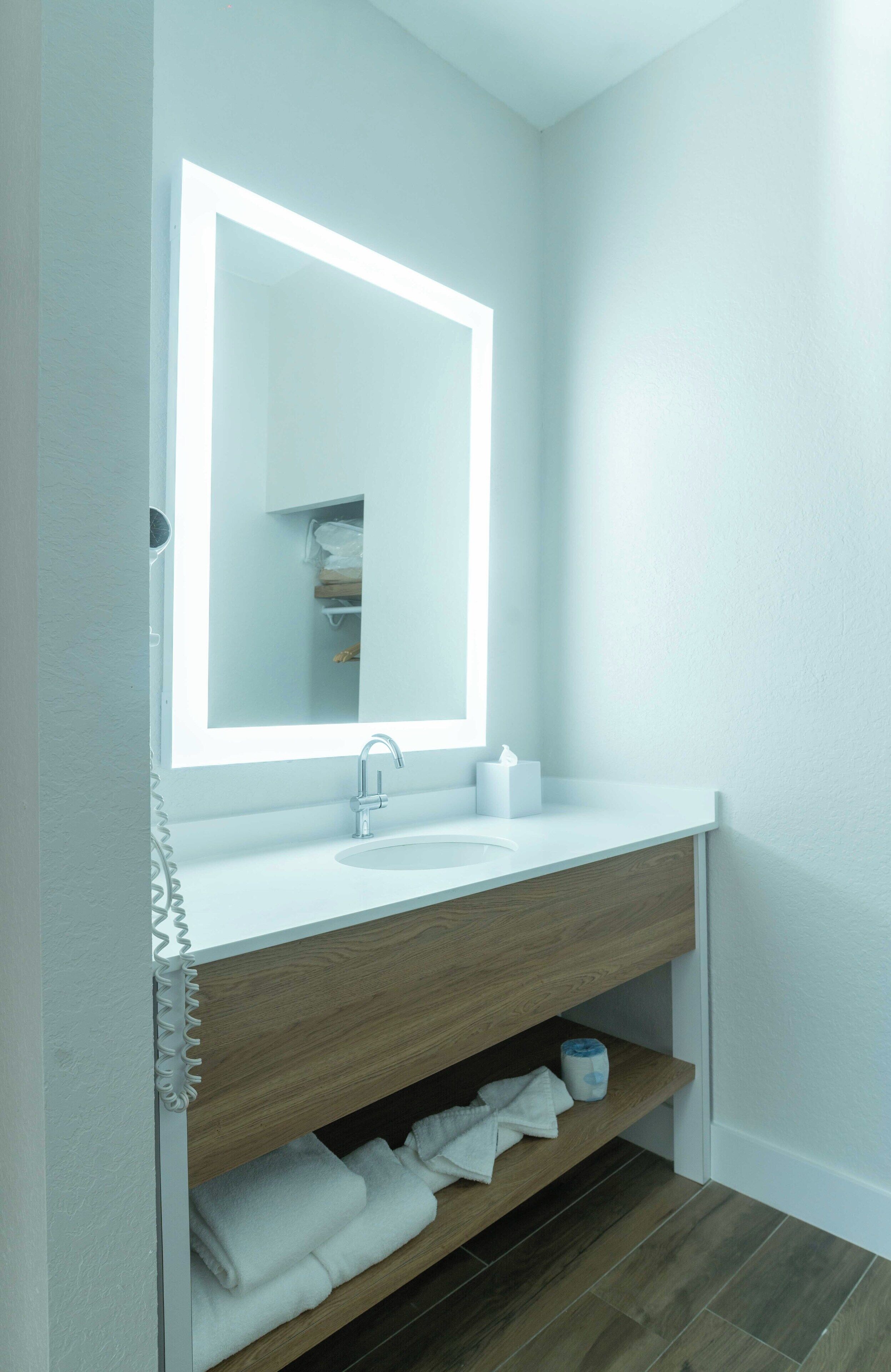 A modern bathroom with a white vanity, a large mirror, and a built-in shelf with towels.