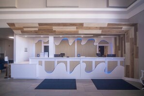 A reception desk with a modern design, a wooden ceiling, and a blue-lit wave pattern on the wall. - Clarion Inn & Suites Central Clearwater Beach (Clearwater)