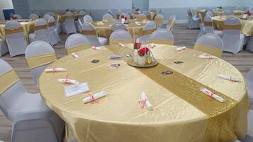 A banquet hall with round tables covered in gold tablecloths, white chairs with gold sashes, and centerpieces with red roses.